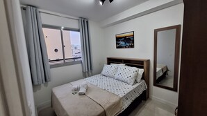 A bedroom with a bed, a window with curtains, a wall-mounted picture, and a mirror. - Seu lindo lar no centro carioca (Rio de Janeiro)