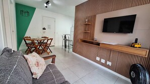 A living room with a sofa, a coffee table, a dining table with chairs, a TV mounted on the wall, and a small shelf with decorative items. - Seu lindo lar no centro carioca (Rio de Janeiro)