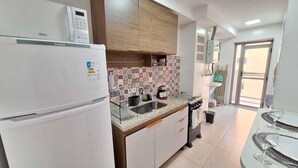 A modern kitchen with a white refrigerator, a tiled backsplash, and a dining area with a table and chairs. - Seu lindo lar no centro carioca (Rio de Janeiro)