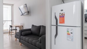 A modern living room with a white refrigerator, a gray sofa, and a dining area with a table and chairs. - LMC 509 (Buenos Aires)