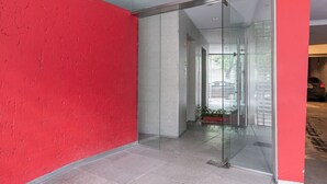A modern interior with a red wall, a glass door leading to a hallway, and a tiled floor. - LMC 509 (Buenos Aires)