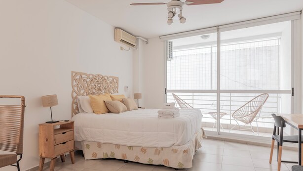 A bedroom with a bed, bedside tables, a ceiling fan, and a large window with a view. - LMC 509 (Buenos Aires)