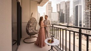 A couple on a balcony with a city view, a hanging chair, and a table with fruits and a bottle. - Chic 1BR Retreat in Business Bay (Dubai)