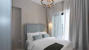 A modern bedroom with a large bed, a nightstand, a lamp, and a view of buildings through sheer curtains. - Chic 1BR Retreat in Business Bay (Dubai)