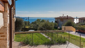 A residential area with a view of a body of water, a paved walkway, and a fenced garden. - Le Terrazze PT36 by Wonderful Italy (Toscolano Maderno)