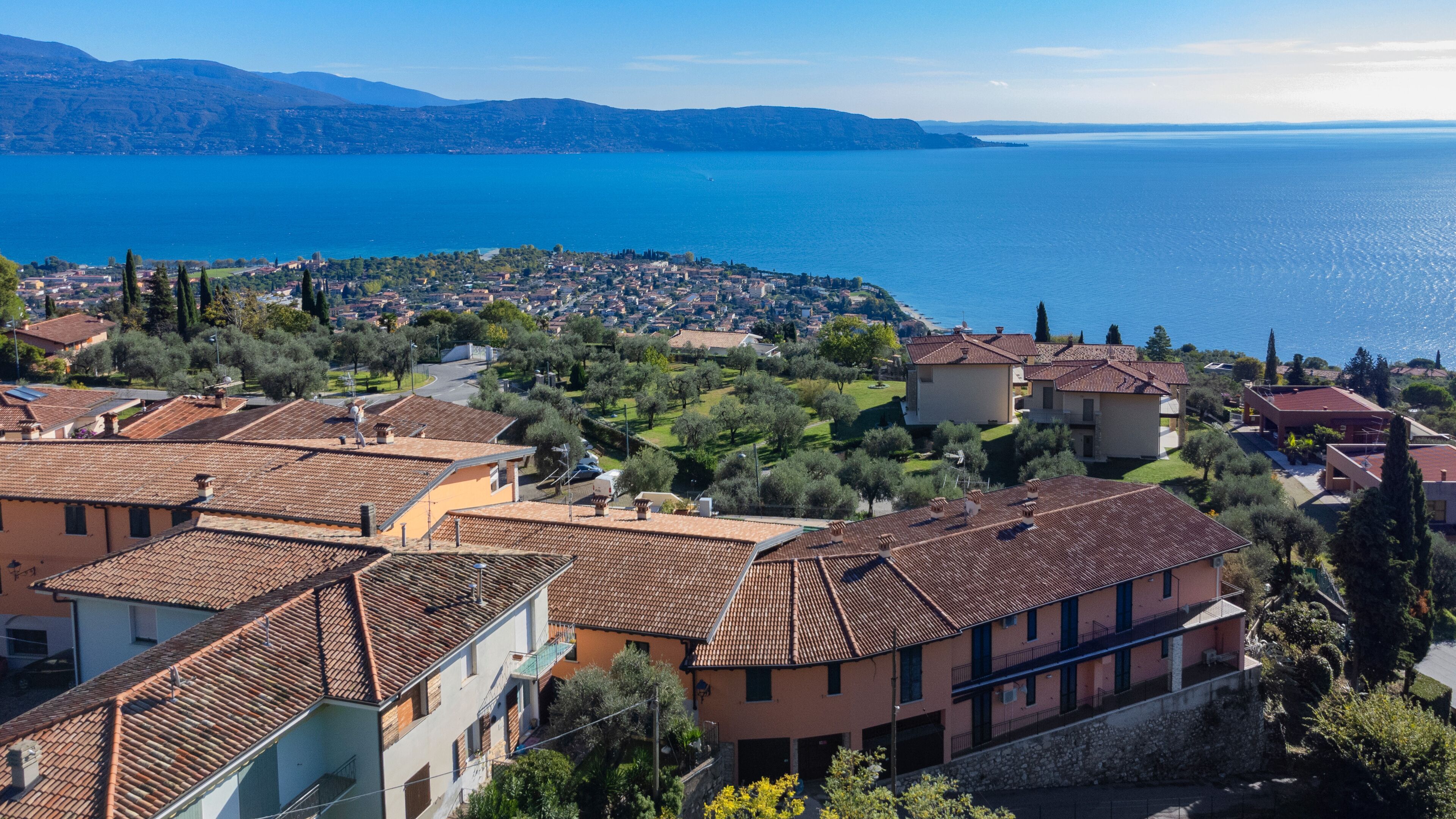A coastal town with terracotta-roofed buildings, a clear view of the sea, and lush greenery.