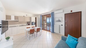 A modern kitchen with white cabinets, a dining table with chairs, and a large window with curtains. - Le Terrazze PT36 by Wonderful Italy (Toscolano Maderno)