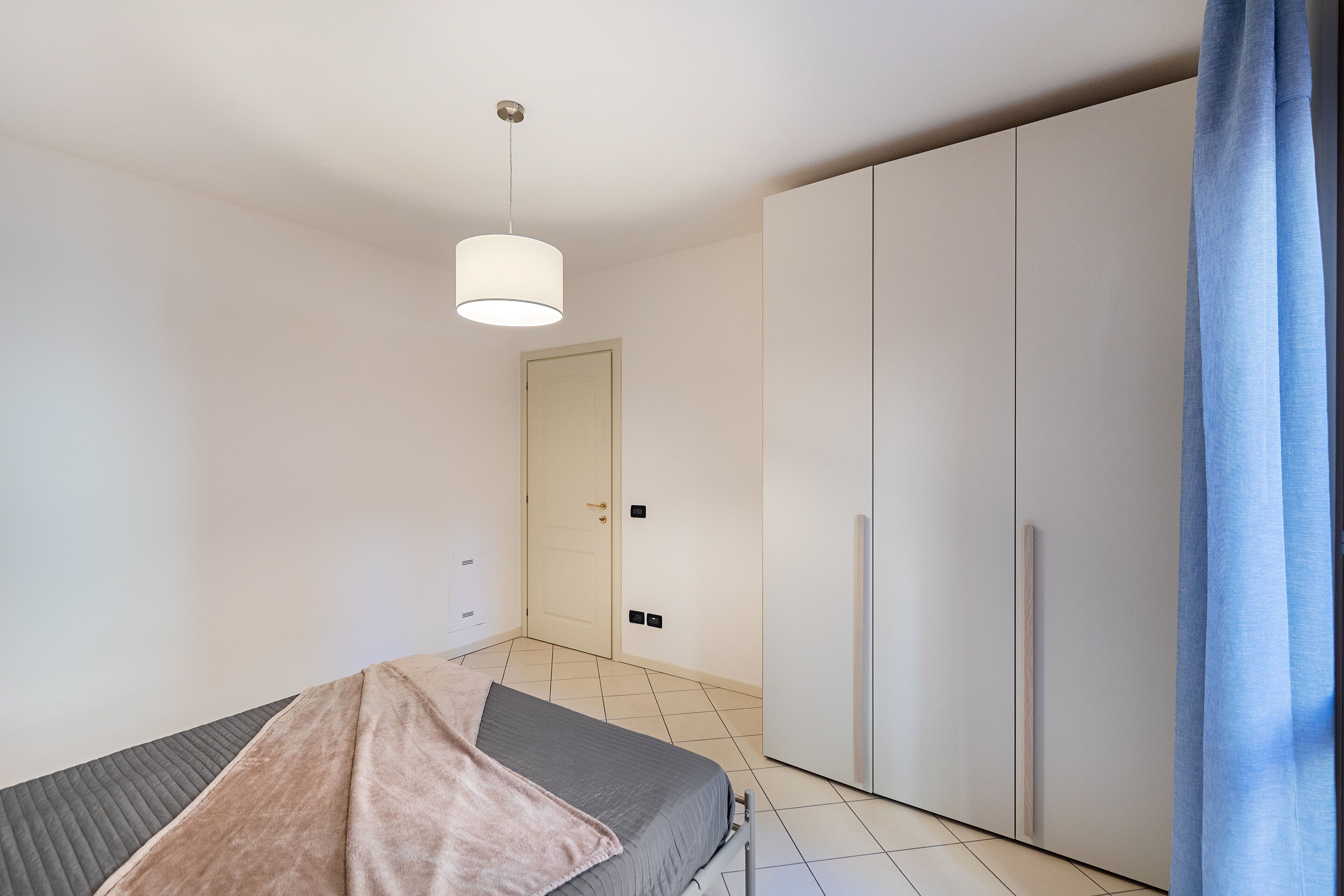 A bedroom with a bed, a wardrobe, and a hanging light fixture.