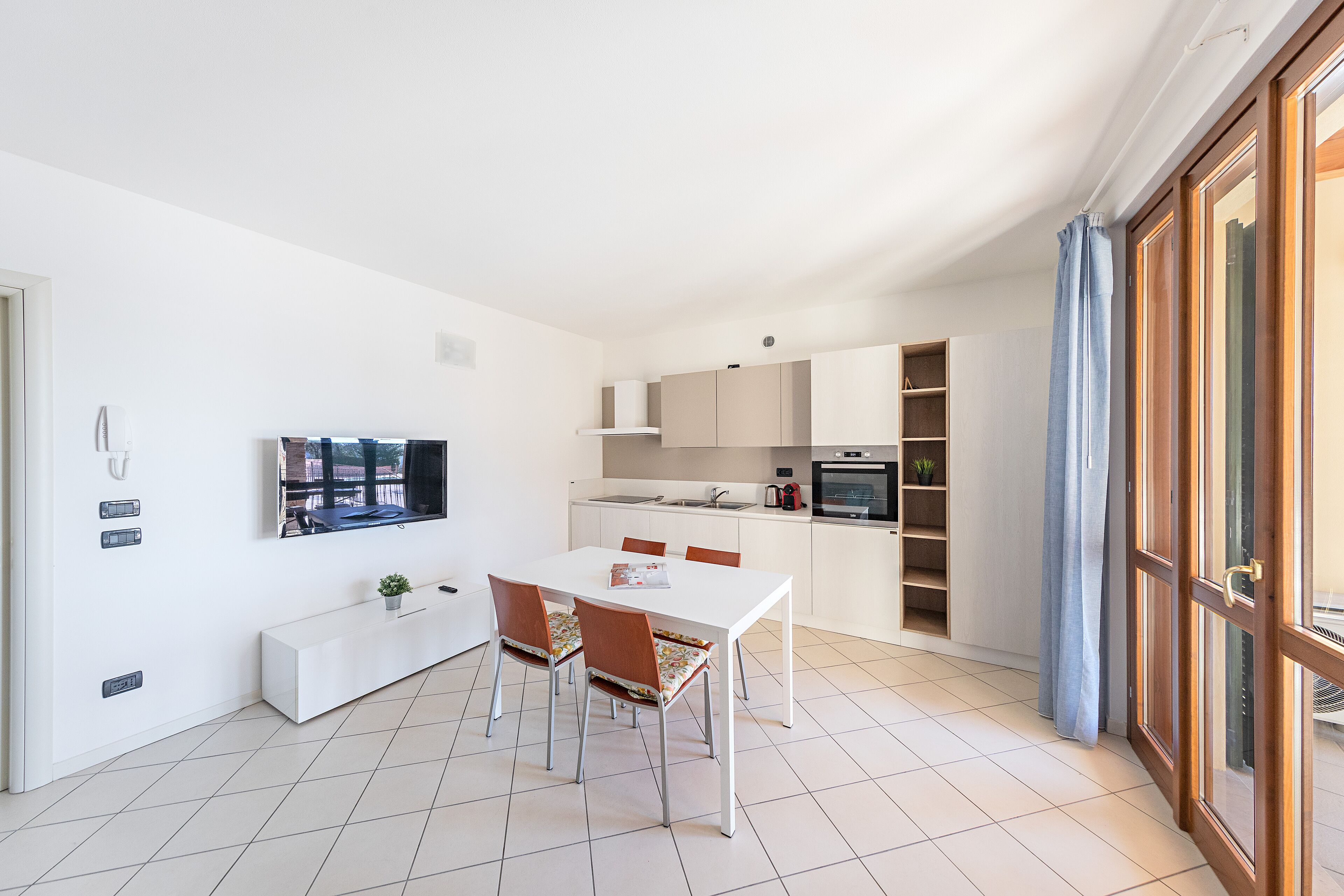 A modern kitchen with white cabinets, a dining table with chairs, and a built-in oven.
