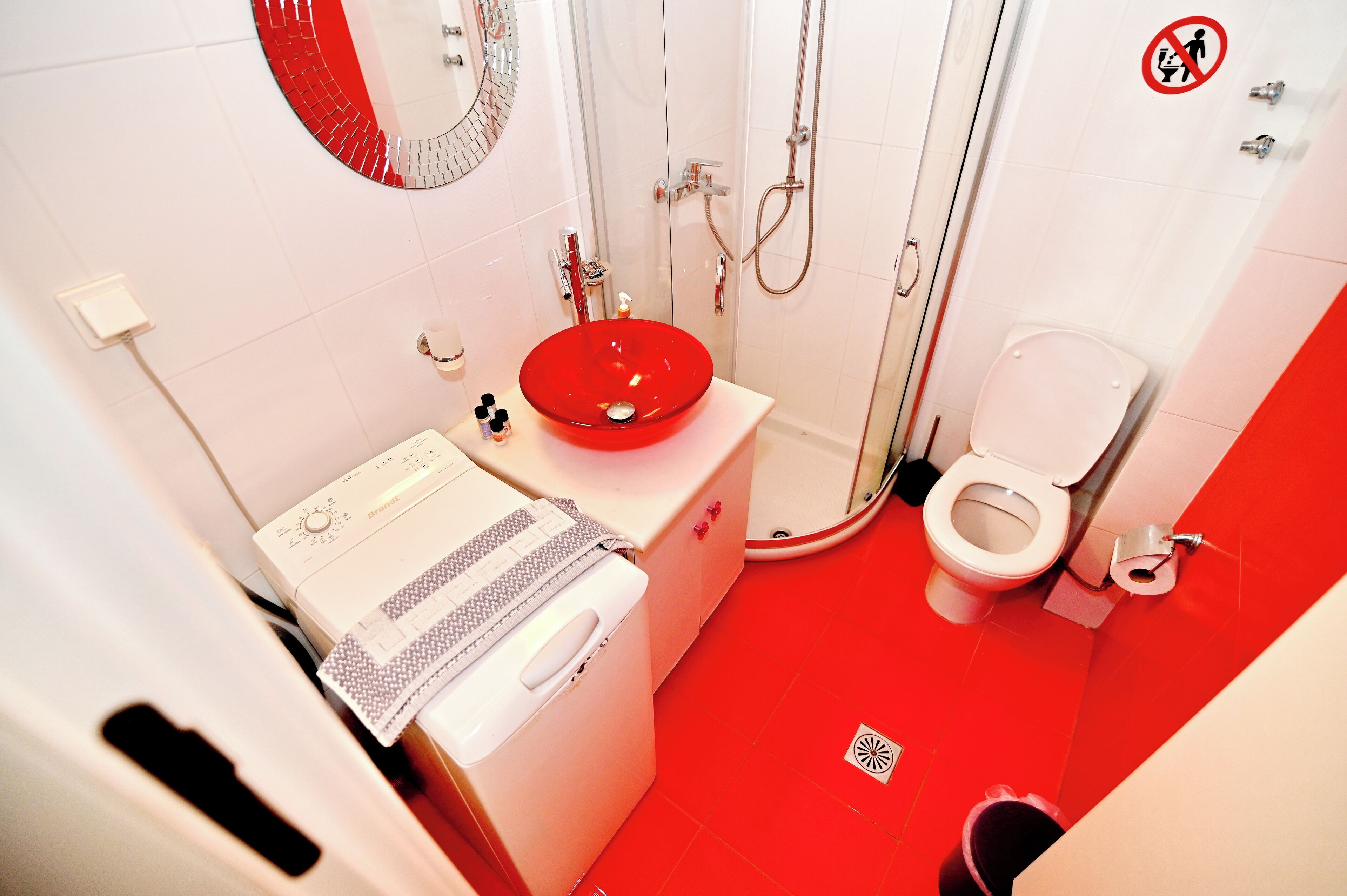 A bathroom with a red sink, white toilet, and a shower area.
