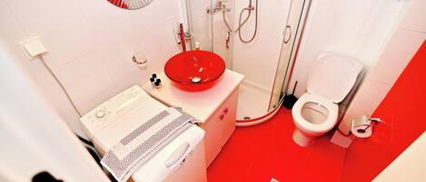 A bathroom with a red sink, white toilet, and a shower area.