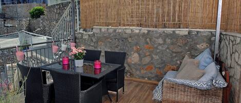 Une terrasse extérieure couverte, dotée d’un mur en pierre, de meubles en osier et de plantes en pot.