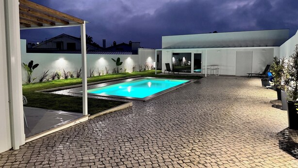 Et moderne poolområde med en belagt terrasse, en rektangulær pool og en bygning med store vinduer.