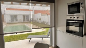 Et moderne køkken med indbygget ovn og mikroovn, samt en skydedør til en patio med pool og udendørs møbler.