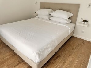 Ein ordentlich bezogenes Bett mit weißen Leinen in einem Raum mit Holzboden und einem beige gefärbten Kopfteil.