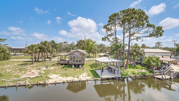 A lakeside property with a dock, a small wooden cabin, and a large tree. - Gulf of Mexico Beach Cottage: Walk to Boat Ramp! (Horseshoe Beach)