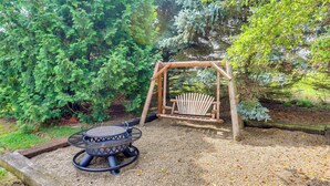 A garden with a wooden swing set, a round table with a metal frame, and a fire pit. - North Fairfield Family Home w/ Hot Tub & Porch! (North Fairfield)