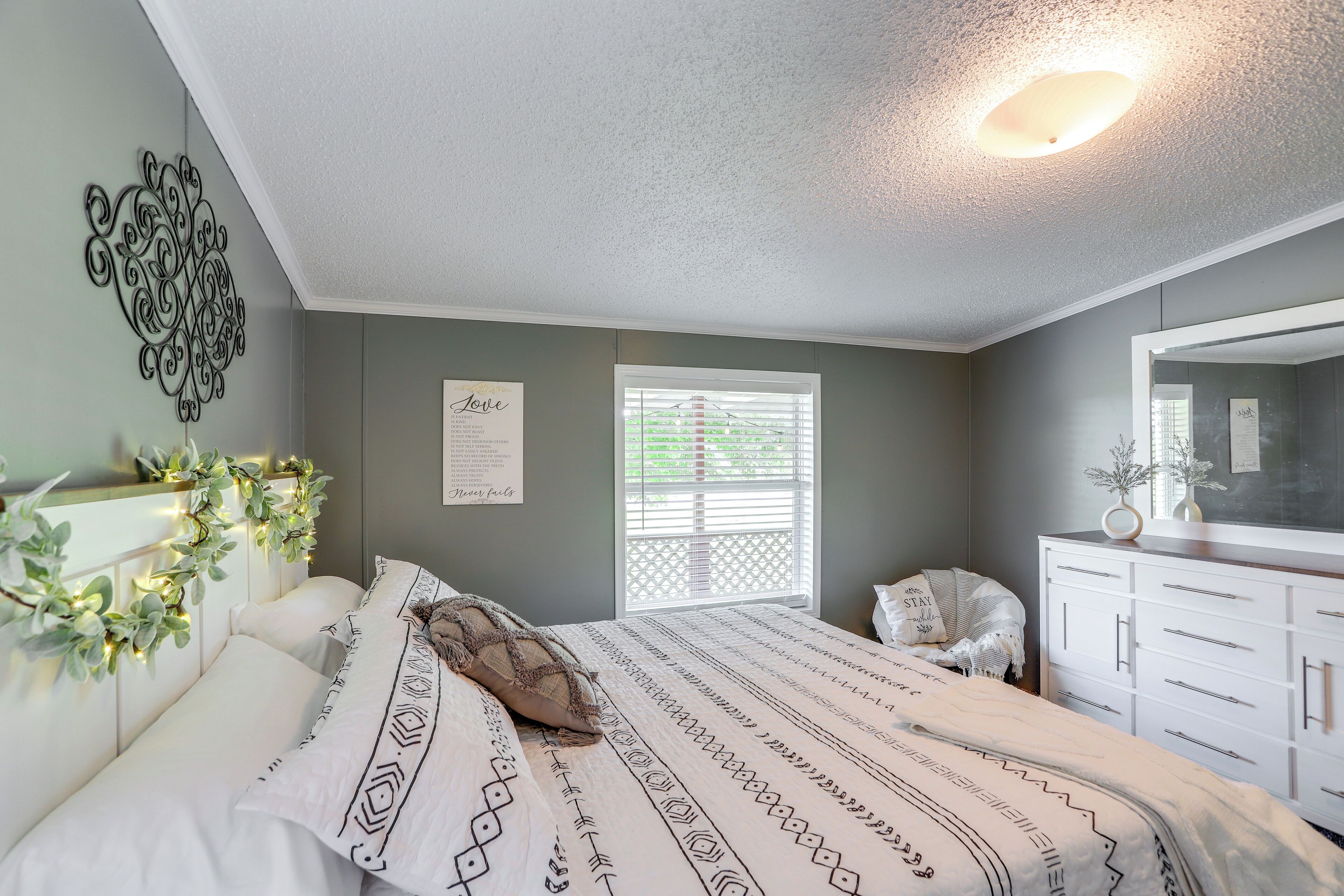 A bedroom with a bed, a dresser, a window with blinds, and a wall decoration.