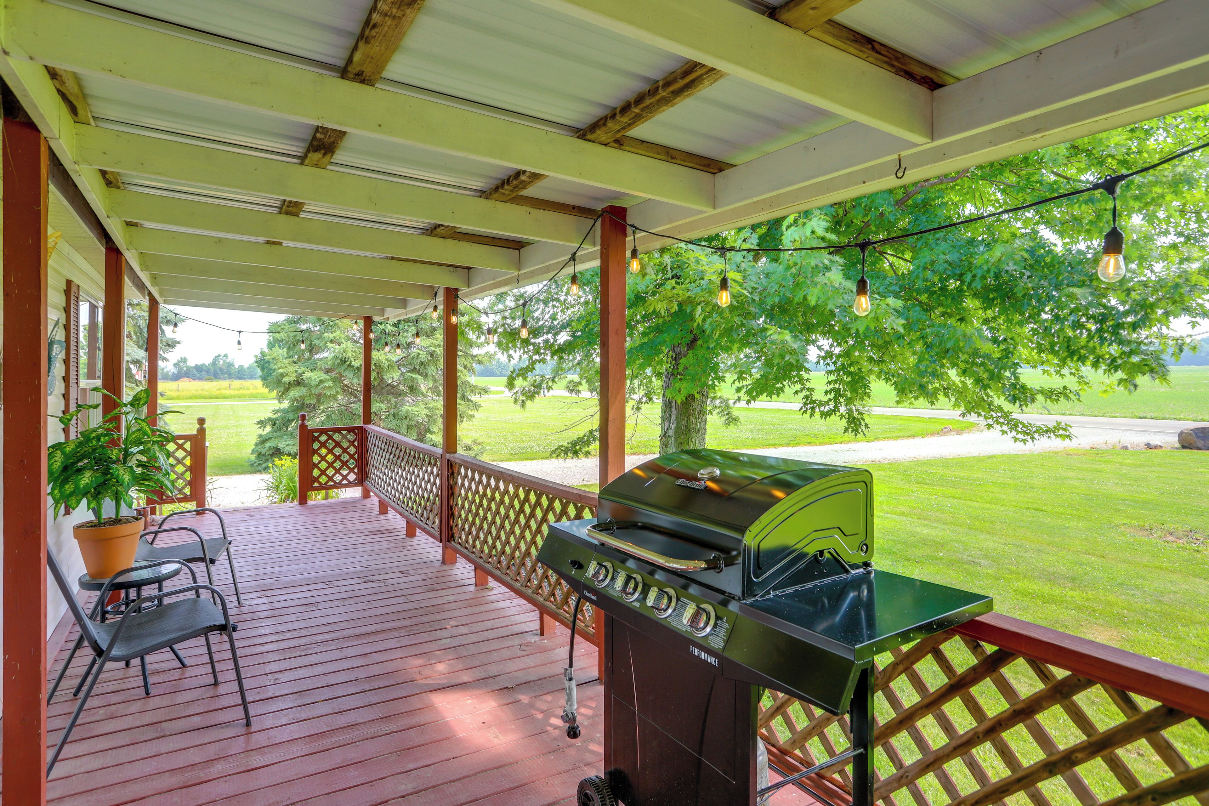 A covered outdoor area with a grill, chairs, and a view of a grassy field.