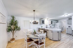 A modern kitchen with white cabinetry, a central island, and a dining area with white chairs. - North Fairfield Family Home w/ Hot Tub & Porch! (North Fairfield)