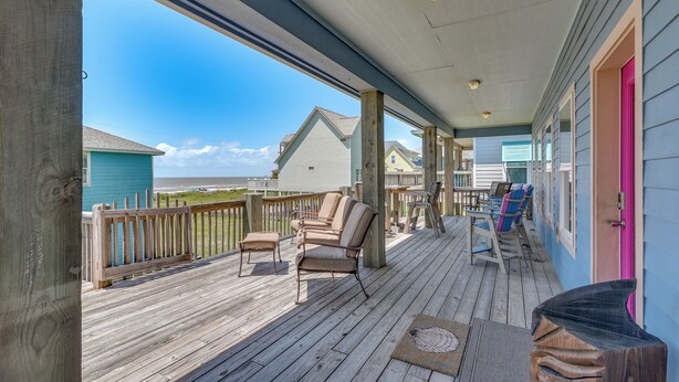 A wooden deck with outdoor furniture, a view of the beach, and a building with a pink door. - Steps to Crystal Beach! Family & Pet-friendly Home (Port Bolivar)