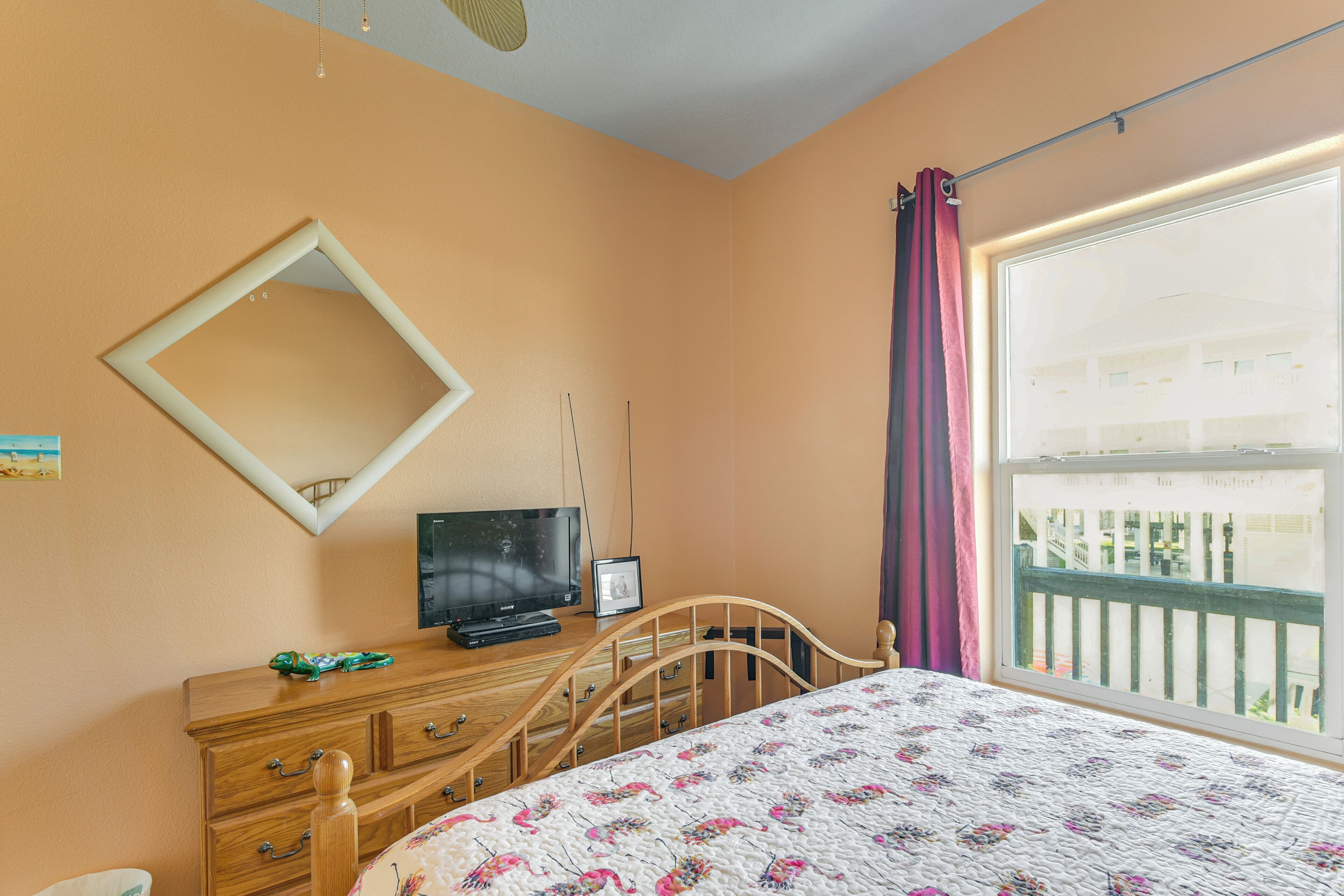 A bedroom with a bed, dresser, television, and a window with curtains.
