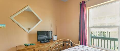 A bedroom with a bed, dresser, television, and a window with curtains.