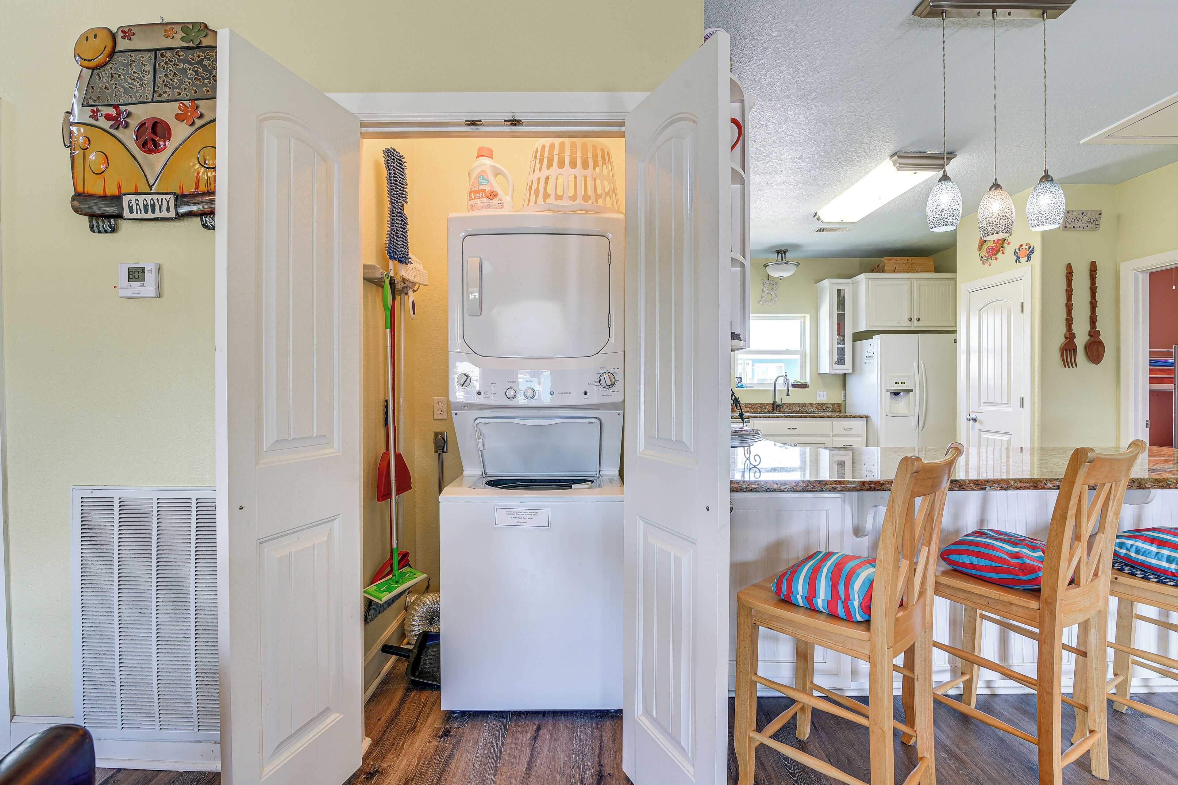 Une cuisine compacte équipée d’un lave-linge et d’un sèche-linge intégrés, de chaises en bois avec des coussins colorés et d’une porte blanche donnant sur une autre pièce.