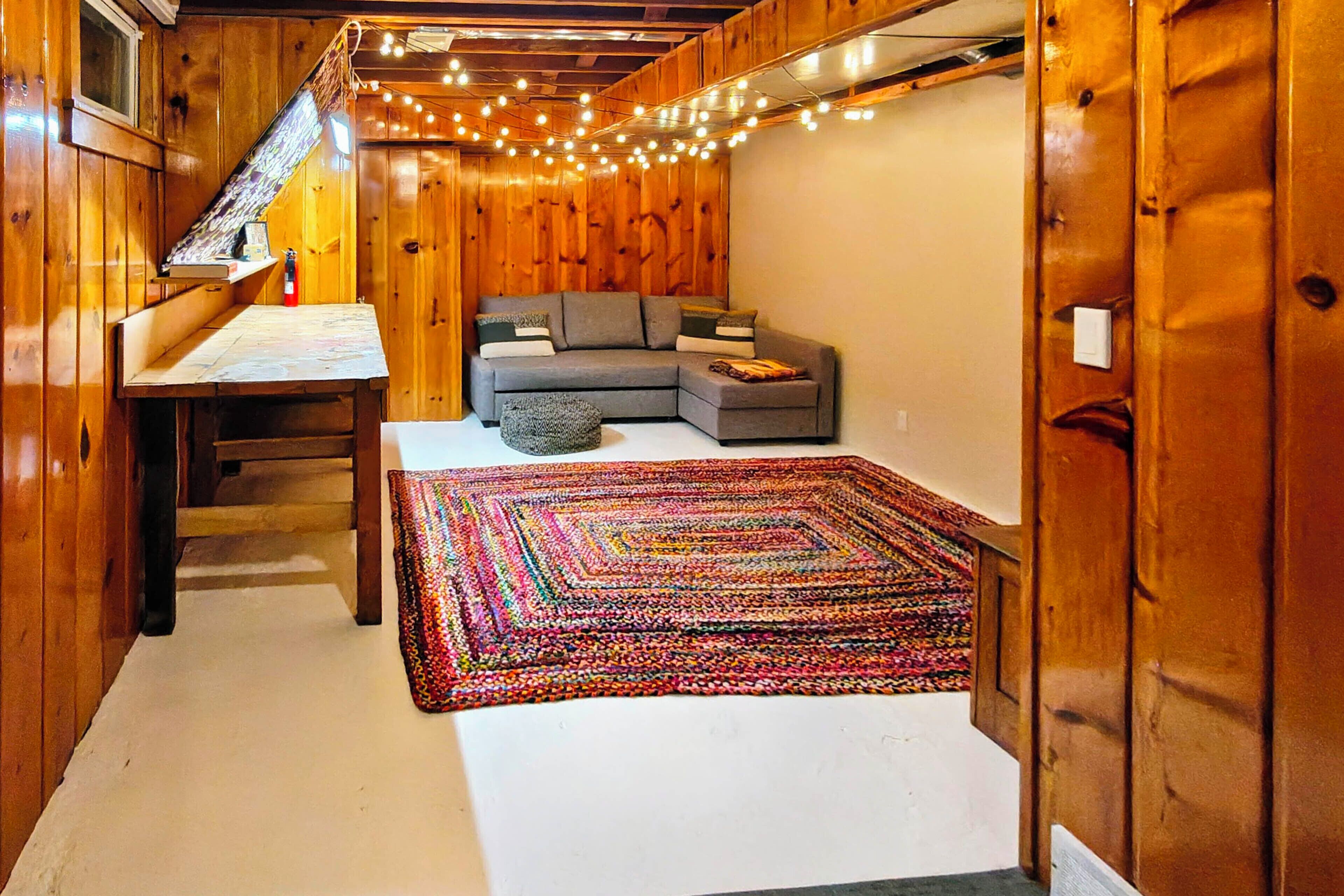 Ein gemütliches Zimmer mit Holzvertäfelung, einem grauen Sofa, einem farbenfrohen Teppich und einem kleinen Tisch.