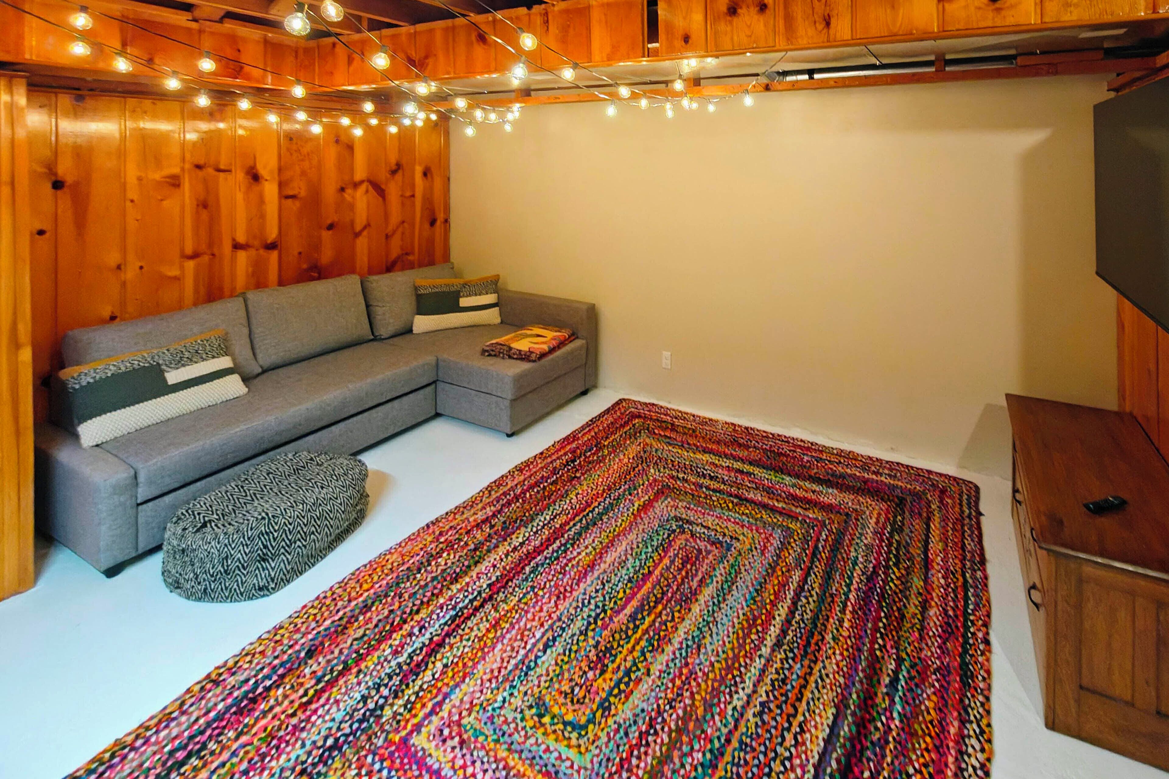 Um quarto aconchegante com um sofá seccional cinza, um tapete tecido colorido e paredes de madeira.