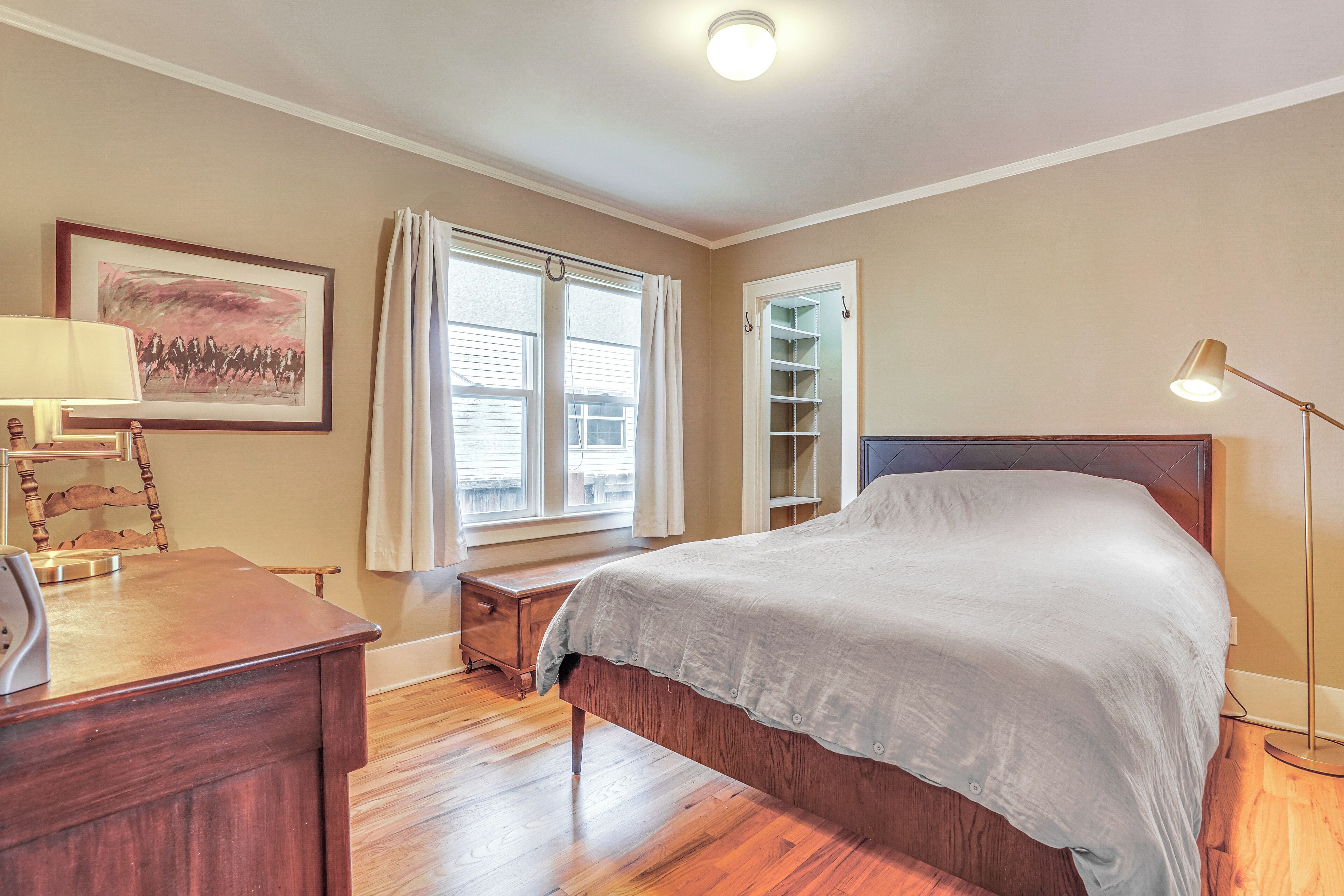 A bedroom with a bed, a desk, a chair, a lamp, a window with curtains, and a shelf.