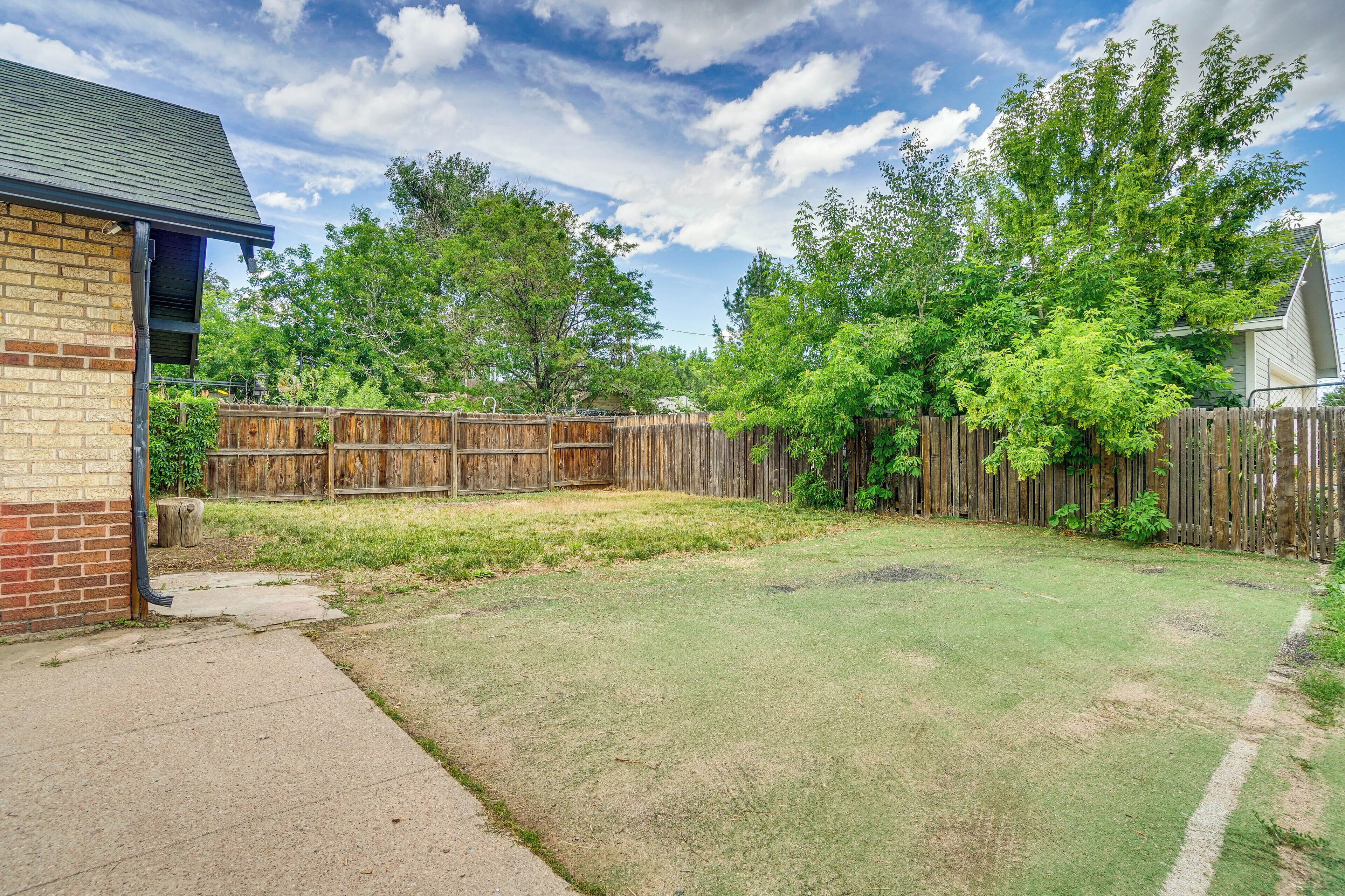 A backyard with a wooden fence, a brick building, and a grassy lawn.