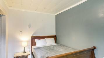 Quarto com cama de madeira, mesa de cabeceira com abajur e parede lisa.