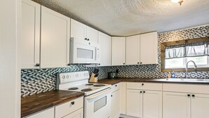 Una cocina con armarios blancos, microondas, estufa y salpicadero de azulejos.