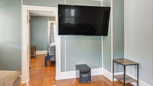 Una habitación con televisión montada, una pequeña mesa y un banco.