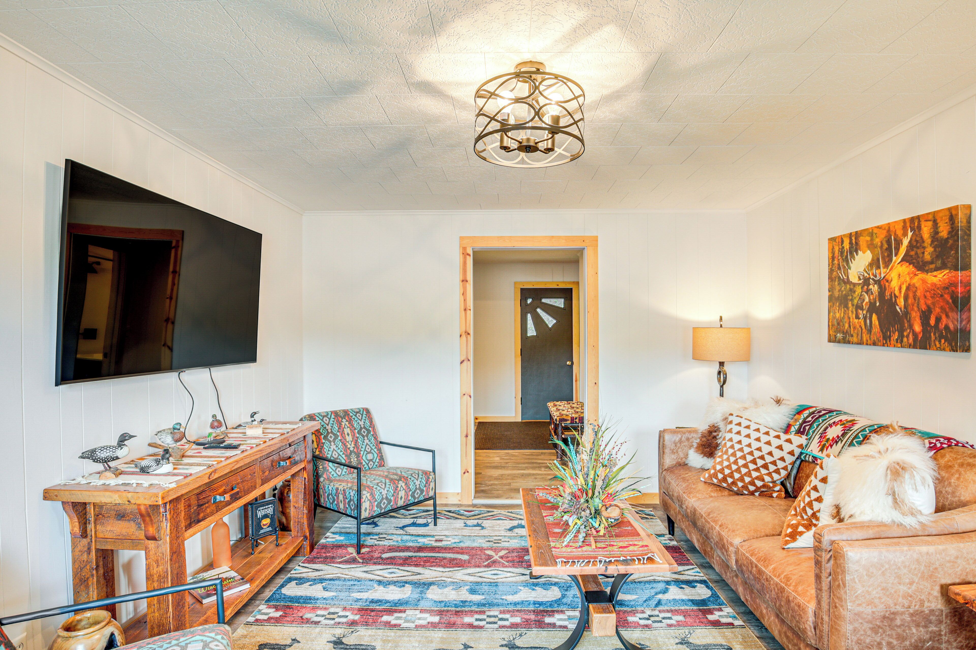 A living room with a wooden coffee table, a sofa, a TV mounted on the wall, and a patterned rug.