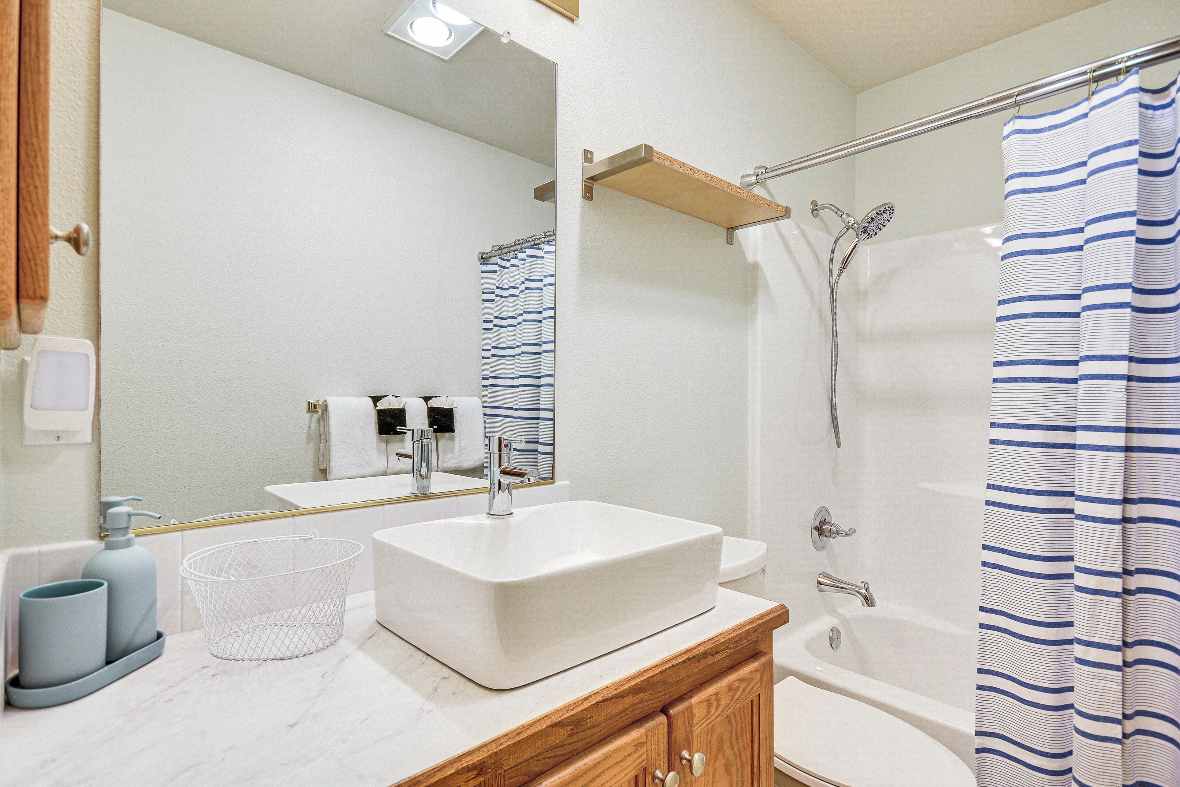A bathroom with a white sink, wooden vanity, and a shower with a striped curtain.