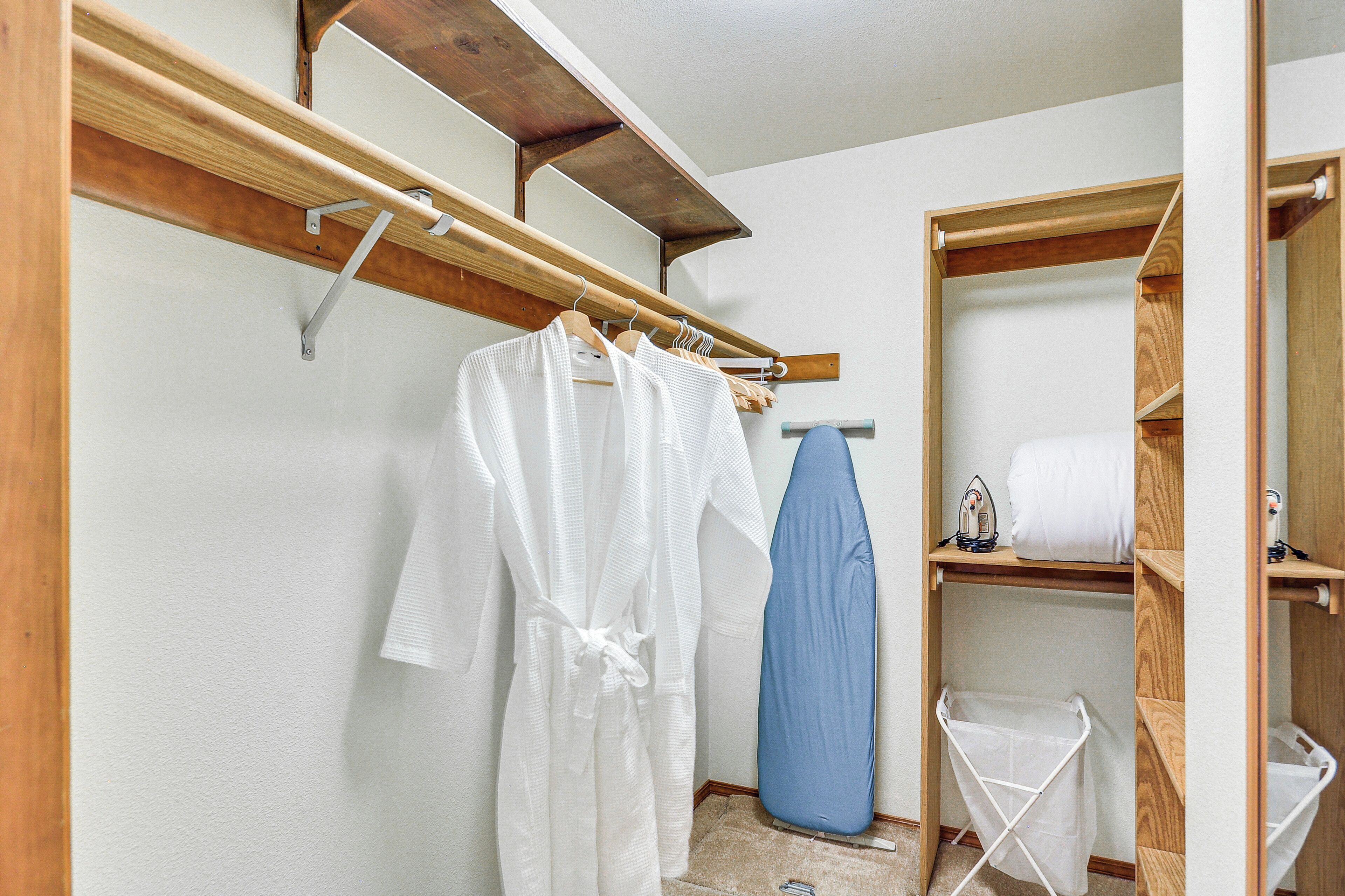 Un baño pequeño con un estante de madera, una bata colgada, una tabla de planchar azul y un tendedero blanco.