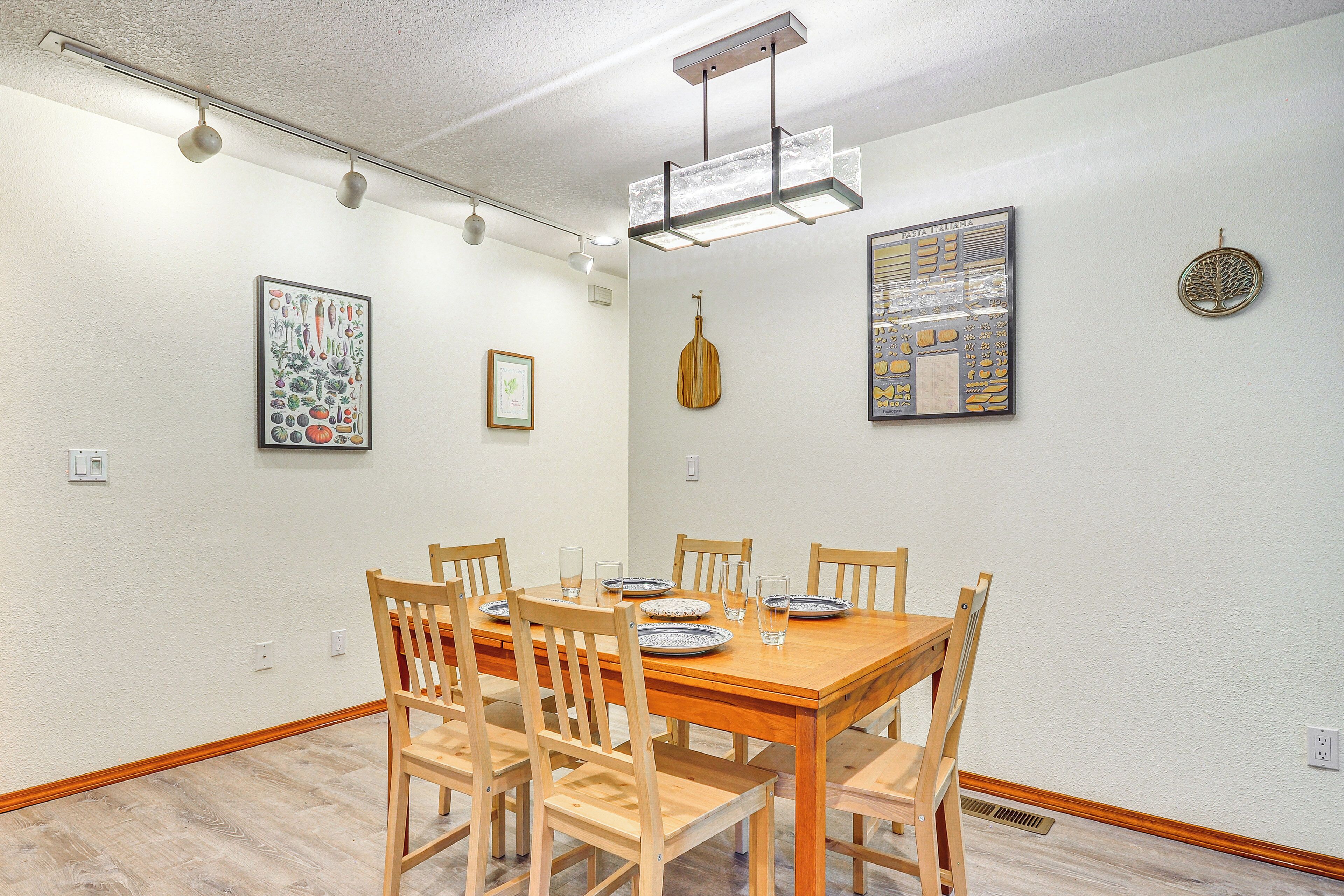 A dining area with a wooden table and chairs, a hanging light fixture, and wall art.