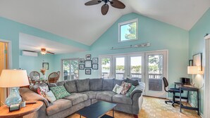 A spacious living room with a large sectional sofa, a coffee table, and a dining area with a table and chairs. There is a ceiling fan, a lamp, and a computer desk with a chair. - Charming Wolcott Cottage w/ Fire Pit & Mini Dock (Wolcott)
