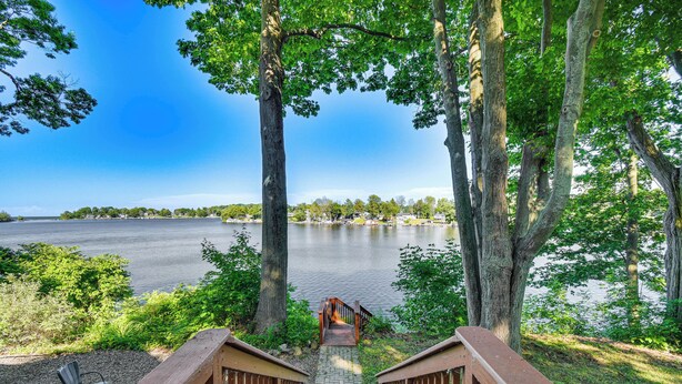 A wooden staircase leading to a dock over a calm lake, surrounded by trees and greenery. - Charming Wolcott Cottage w/ Fire Pit & Mini Dock (Wolcott)