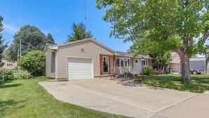 A single-story house with a garage, a front yard with grass and a tree, and a clear blue sky. - Walk to Park: Waterloo Home w/ Furnished Deck (Waterloo)