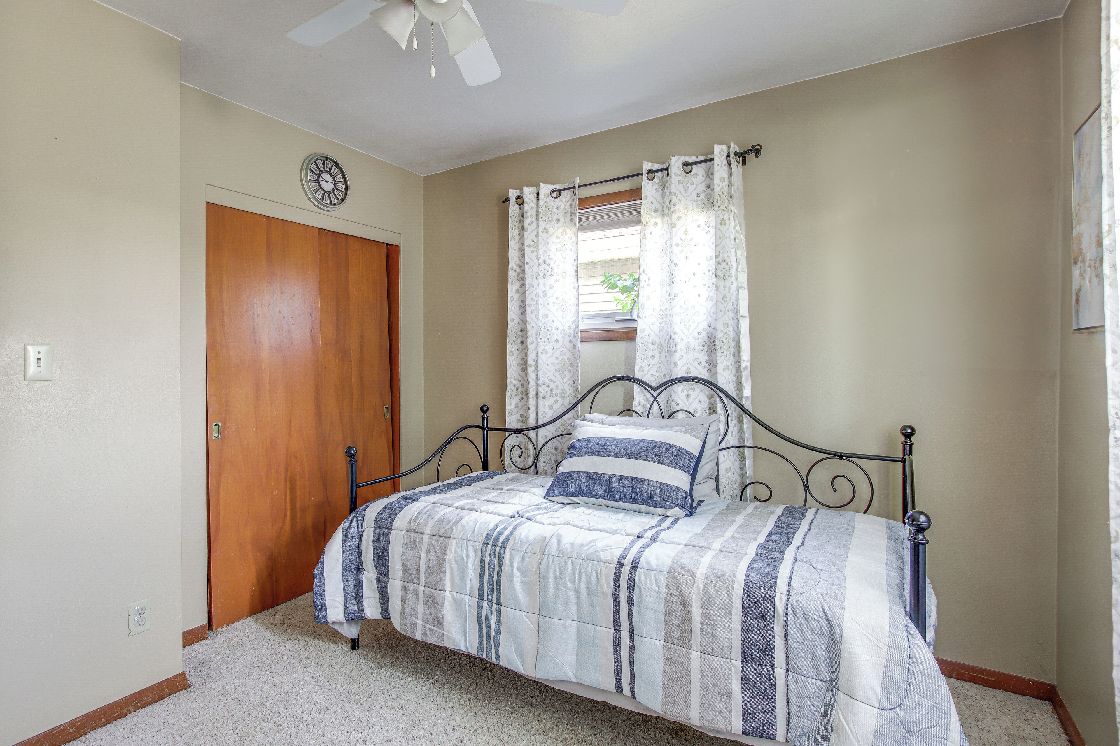A bedroom with a bed, a wooden door, a ceiling fan, and a window with curtains.