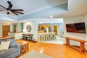 Amplia sala de estar con sofá, mesa de centro y mesa de comedor. Se observa una cocina con barra y taburetes al fondo.