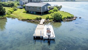 A house with a dock extending into a calm lake, surrounded by greenery and a clear sky. - Sweet Family Cottage on Beautiful Potter's Pond in East Matunuck (South Kingstown)