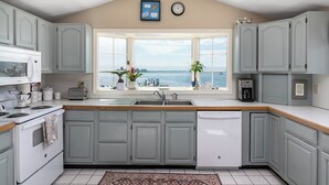 A kitchen with grey cabinets, a white stove, a sink, and a view of the sea. - Sweet Family Cottage on Beautiful Potter's Pond in East Matunuck (South Kingstown)