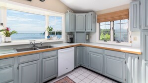 A kitchen with light blue cabinets, a dishwasher, a sink, and a window with a view of the sea. - Sweet Family Cottage on Beautiful Potter's Pond in East Matunuck (South Kingstown)