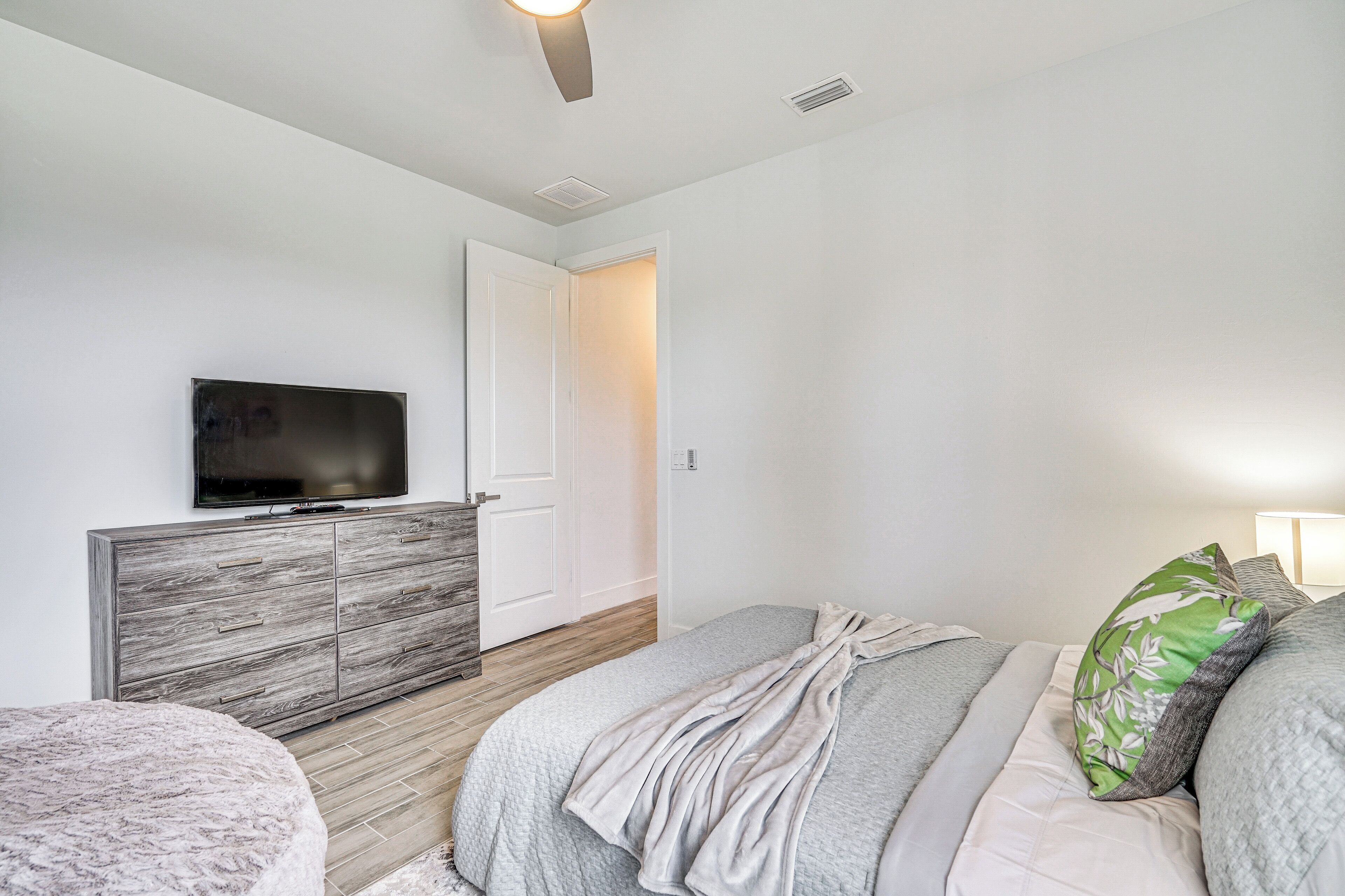 Une chambre à coucher avec un lit, un téléviseur posé sur une commode en bois, une porte et une lampe.