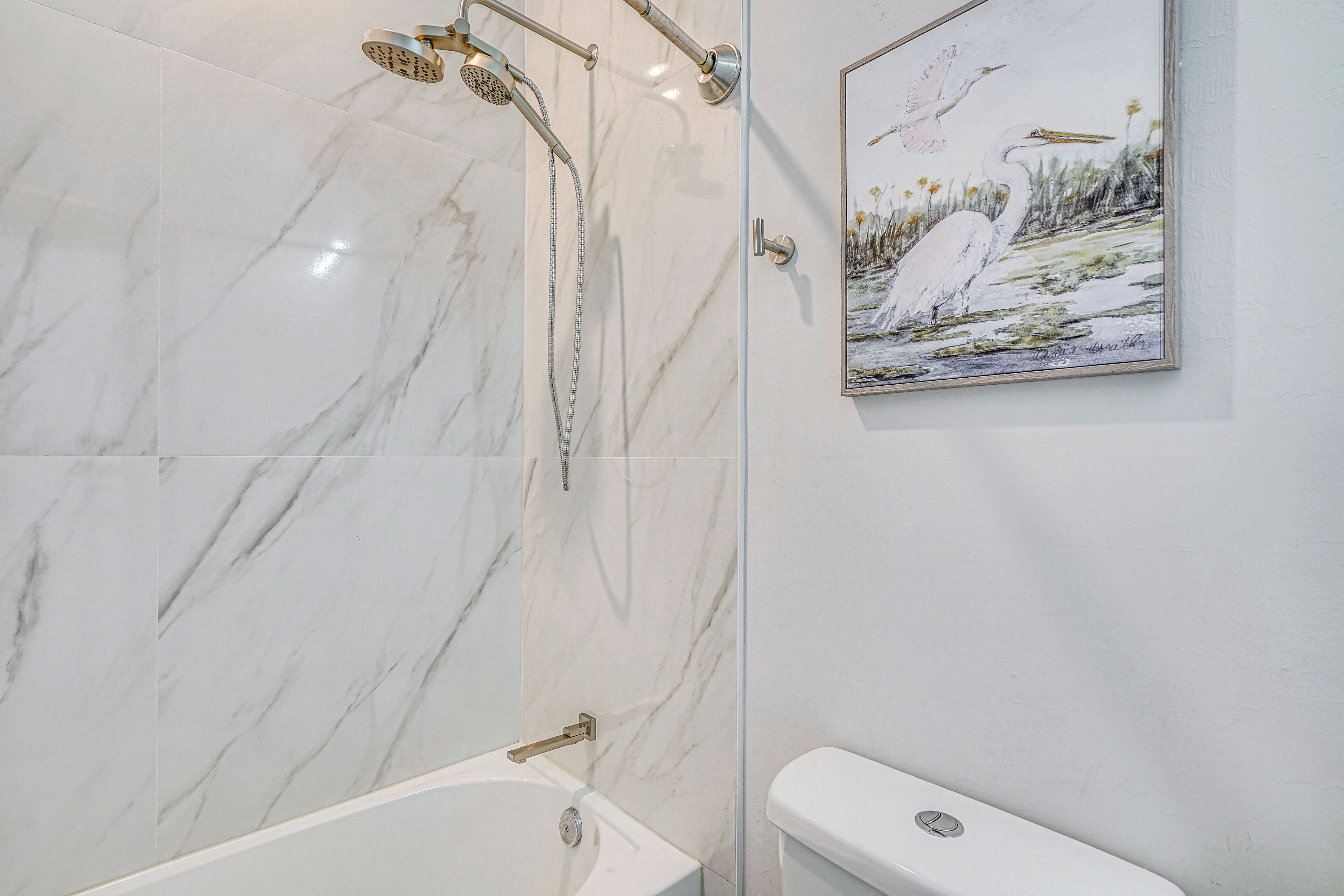 Un baño con pared de mármol, una bañera, un inodoro y un cuadro con pájaros.