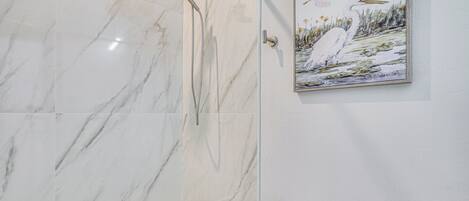 Un baño con pared de mármol, una bañera, un inodoro y un cuadro con pájaros.